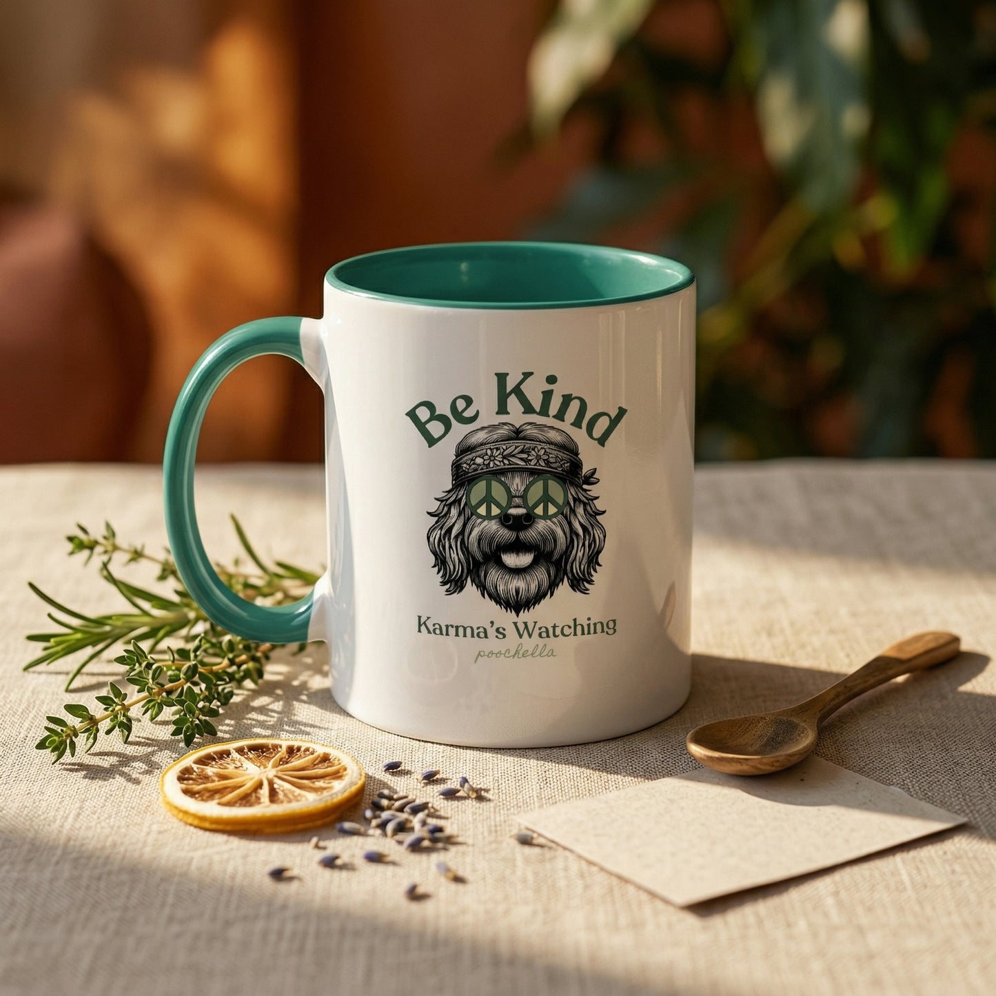 Mug with 'Be Kind Karma is Watching' text and graphic on a table with dried herbs and a spoon.