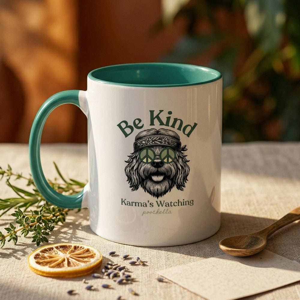Mug with 'Be Kind Karma is Watching' text and graphic on a table with dried herbs and a spoon.