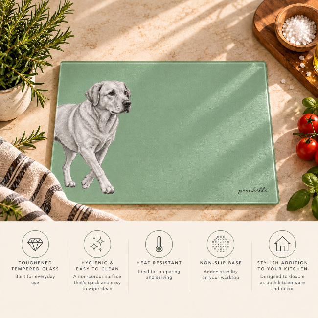 A rectangular green glass cutting board with an Labrador dog illustration and the name 'poochella' in script, styled on a kitchen countertop with herbs, tomatoes, a cloth, and a wooden bowl of salt. A feature summary banner runs along the bottom with icons for toughness, cleanliness, heat resistance, non-slip base, and kitchen decor appeal.