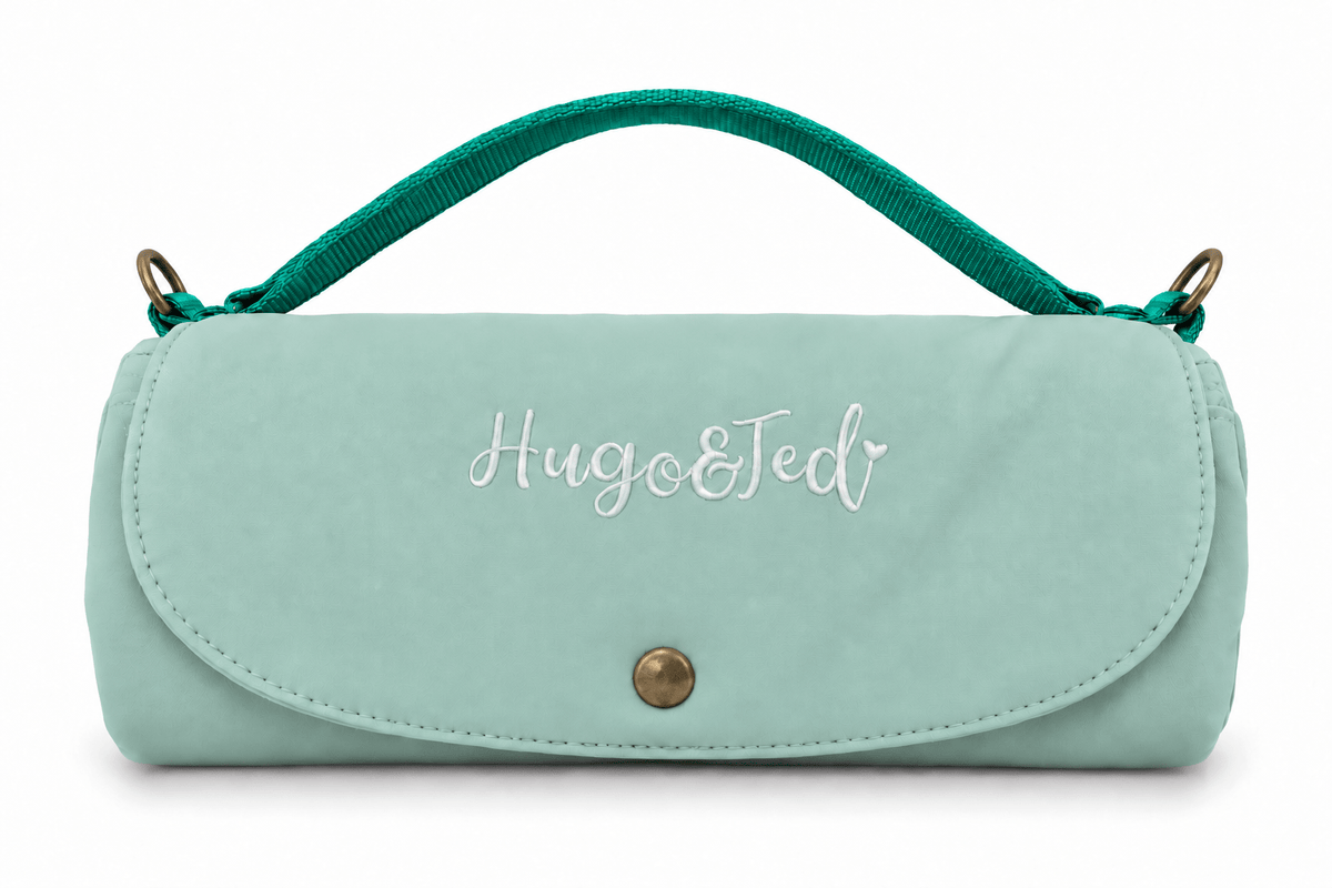 A mint green nylon handbag with a top handle, featuring the embroidered text 'Hugo&Ted' on the front flap and a gold snap button closure, set against a plain white background.