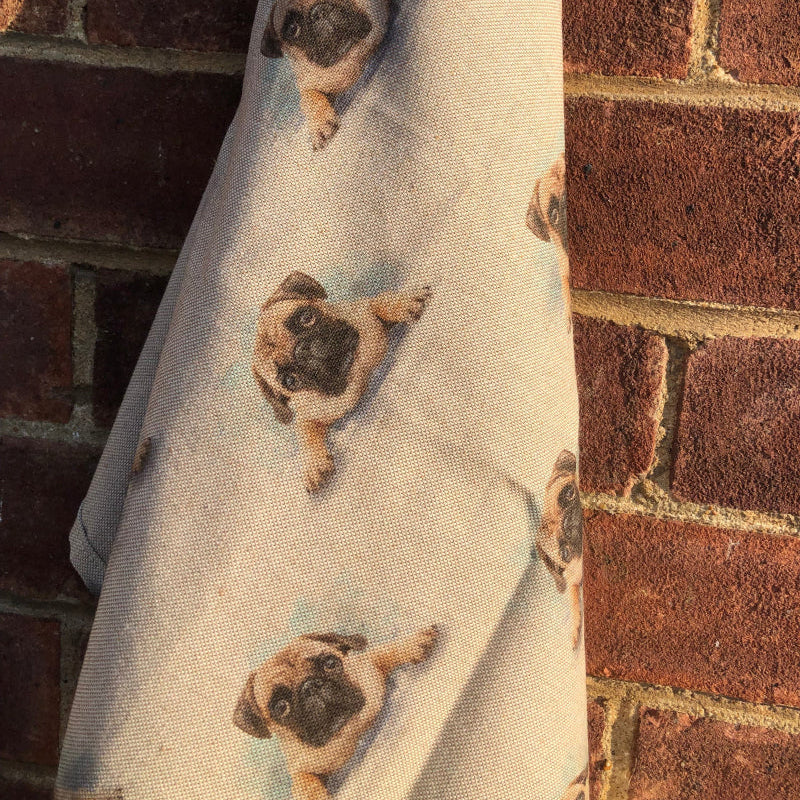Towel with pug dog pattern hanging against a brick wall