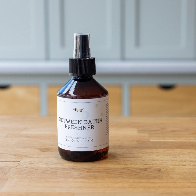 A bottle of Ollie & Co dog freshener spray with Rosemary & Mint essential oils, placed on a wooden surface.