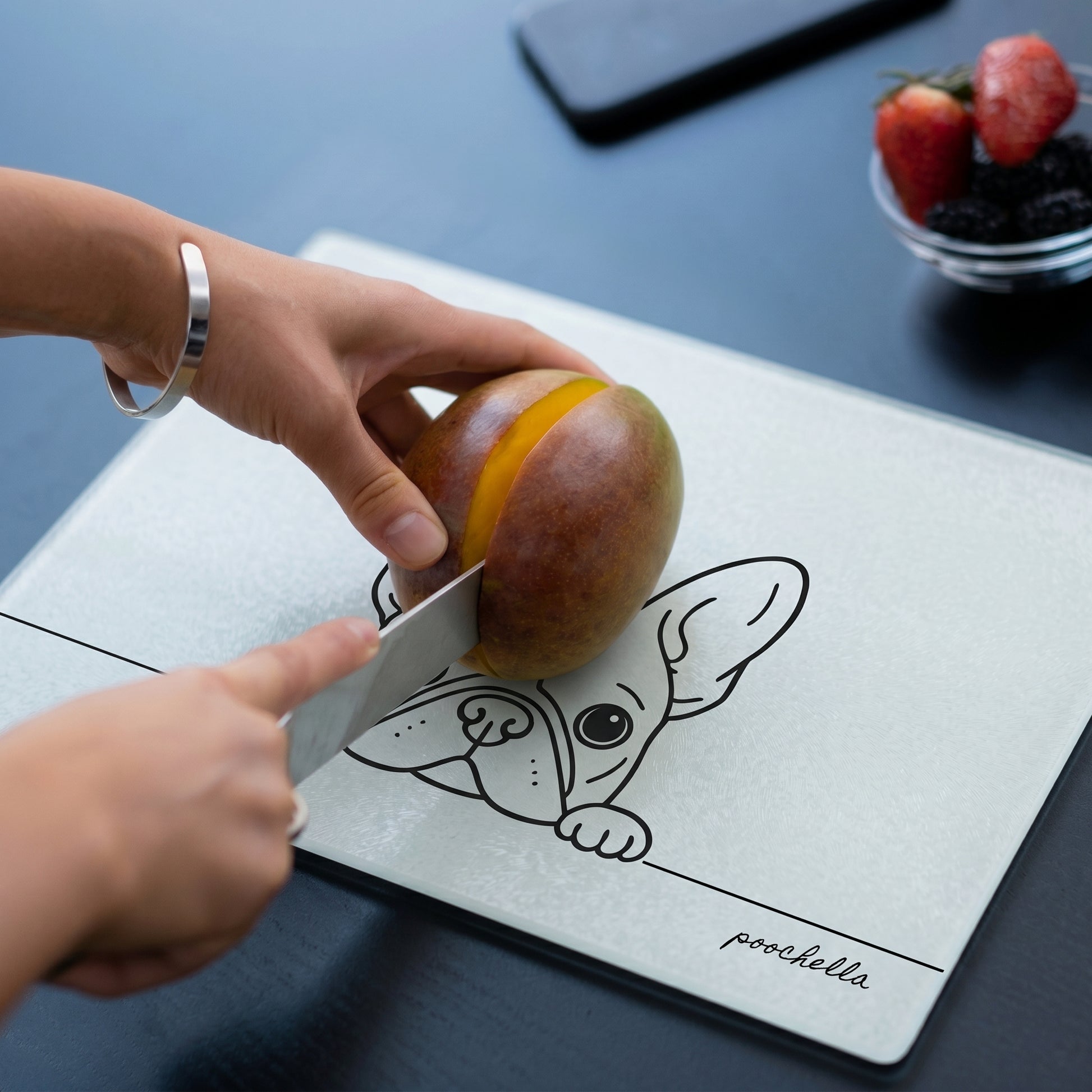 Person cutting a mango on a cutting board with a french bulldog illustration