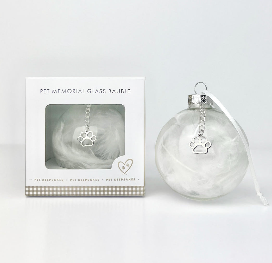 Pet memorial glass bauble with paw charm and packaging on a light gray background