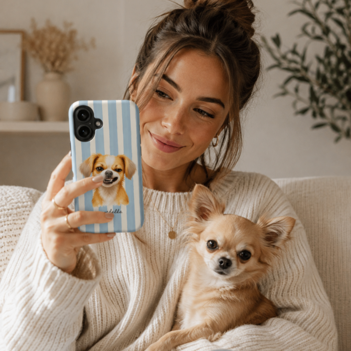 A woman in a cream knit sweater holds a light blue striped phone case featuring a printed chihuahua portrait. A small tan chihuahua sits on her lap in a cozy indoor setting.