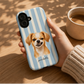  a phone case with a chihuahua portrait printed on it, featuring light blue and white vertical stripes. hand holding the case near a cup of coffee