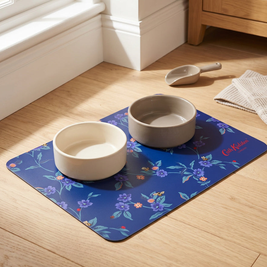 Two ceramic bowls on a floral mat with a wooden cabinet and window in the background