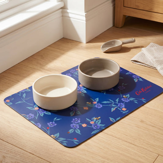 Two ceramic bowls on a floral mat with a wooden cabinet and window in the background