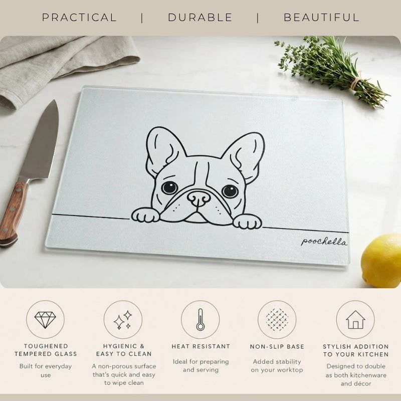 A rectangular glass cutting board with a black line-art illustration of a French bulldog and the name 'poochella' printed on it, styled on a white surface with a knife, herbs, and a lemon. Text at the top reads 'PRACTICAL | DURABLE | BEAUTIFUL' and feature callouts appear along the bottom.