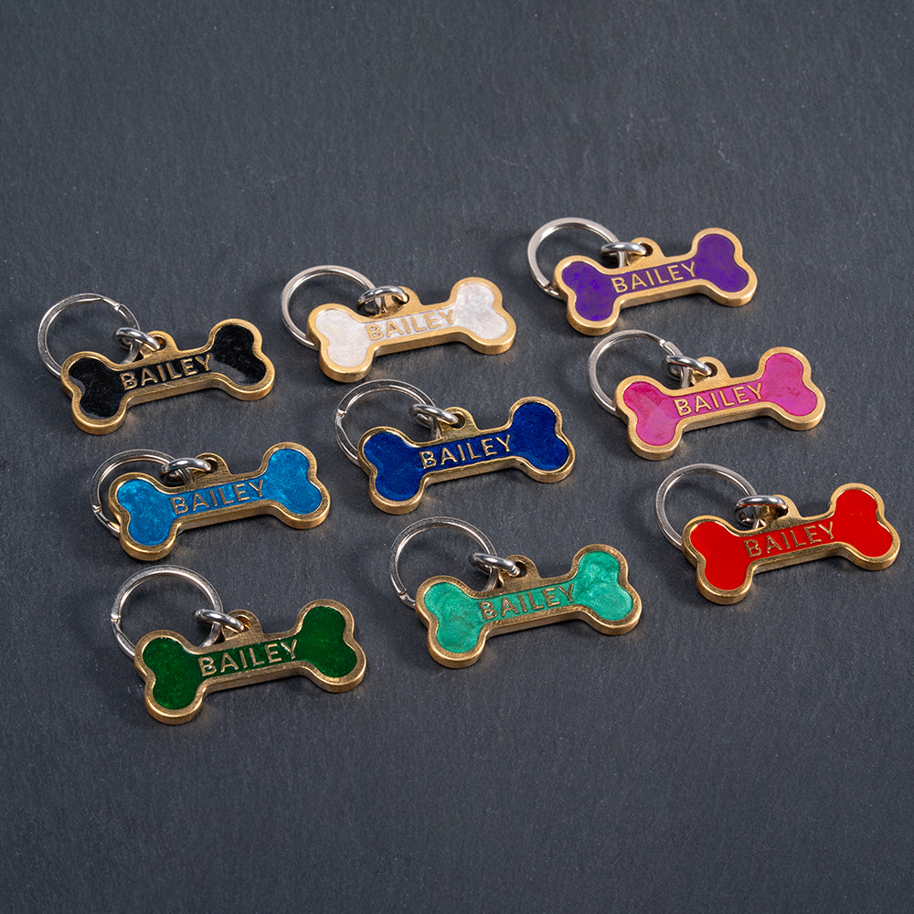 Colorful bone-shaped pet tags with 'BAILEY' engraved on a dark background