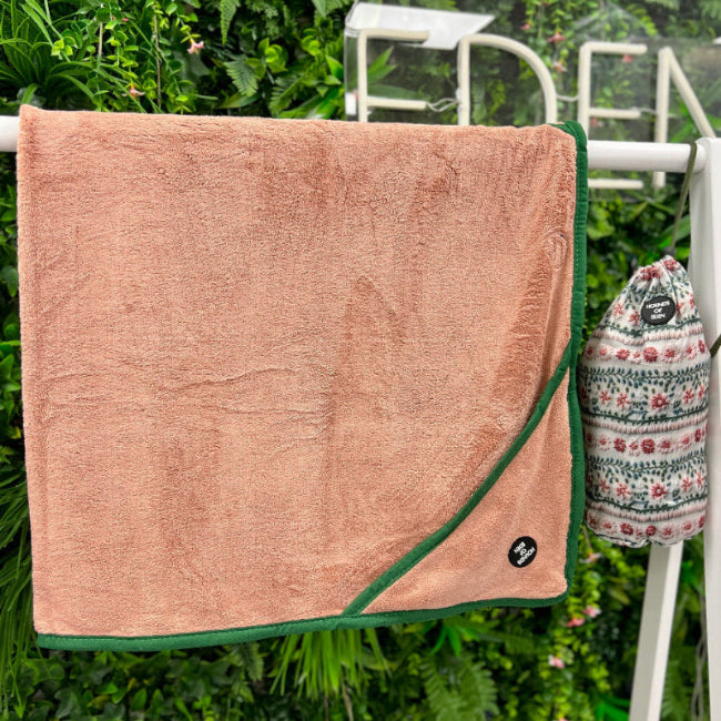 Pink towel with green trim hanging on a clothesline with a floral bag in the background.