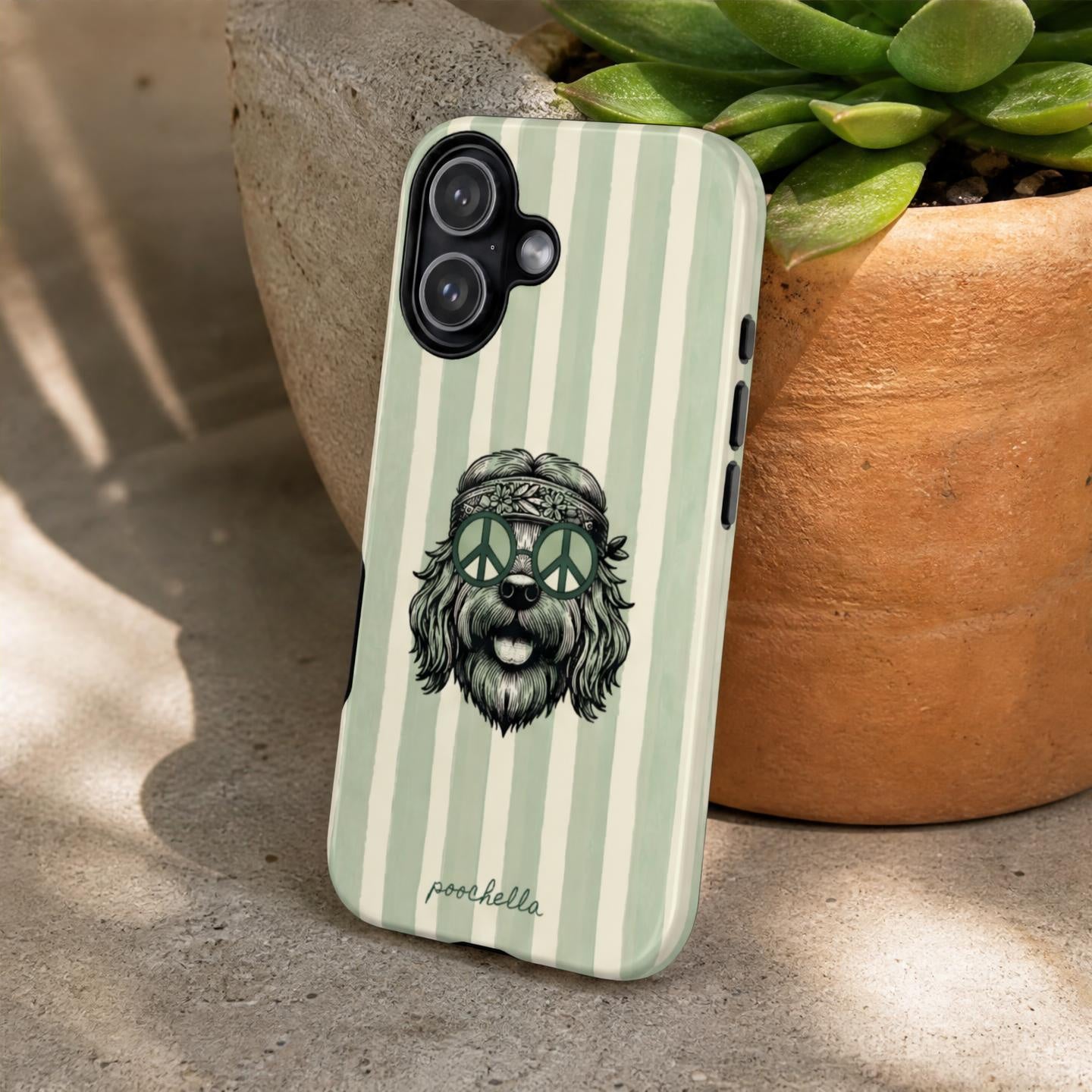 A phone case with a green and white striped background and a cartoon dog wearing peace signs for sunglasses, leaning against a stone surface next to a potted succulent.