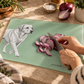 A mint green cutting board with a black-and-white illustration of a dog and the name 'poochella' in script, shown on a kitchen counter while a person slices a red onion with a knife.