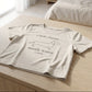 Beige t-shirt with text and dog illustration on a wooden surface in a bedroom.