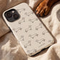 A cream-colored phone case with a black outline print of dachshunds, shown on a phone and placed on a beige linen blanket next to a brown dog's paw.