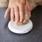 Small dog paw being held by a hand on a white clay with a dark background