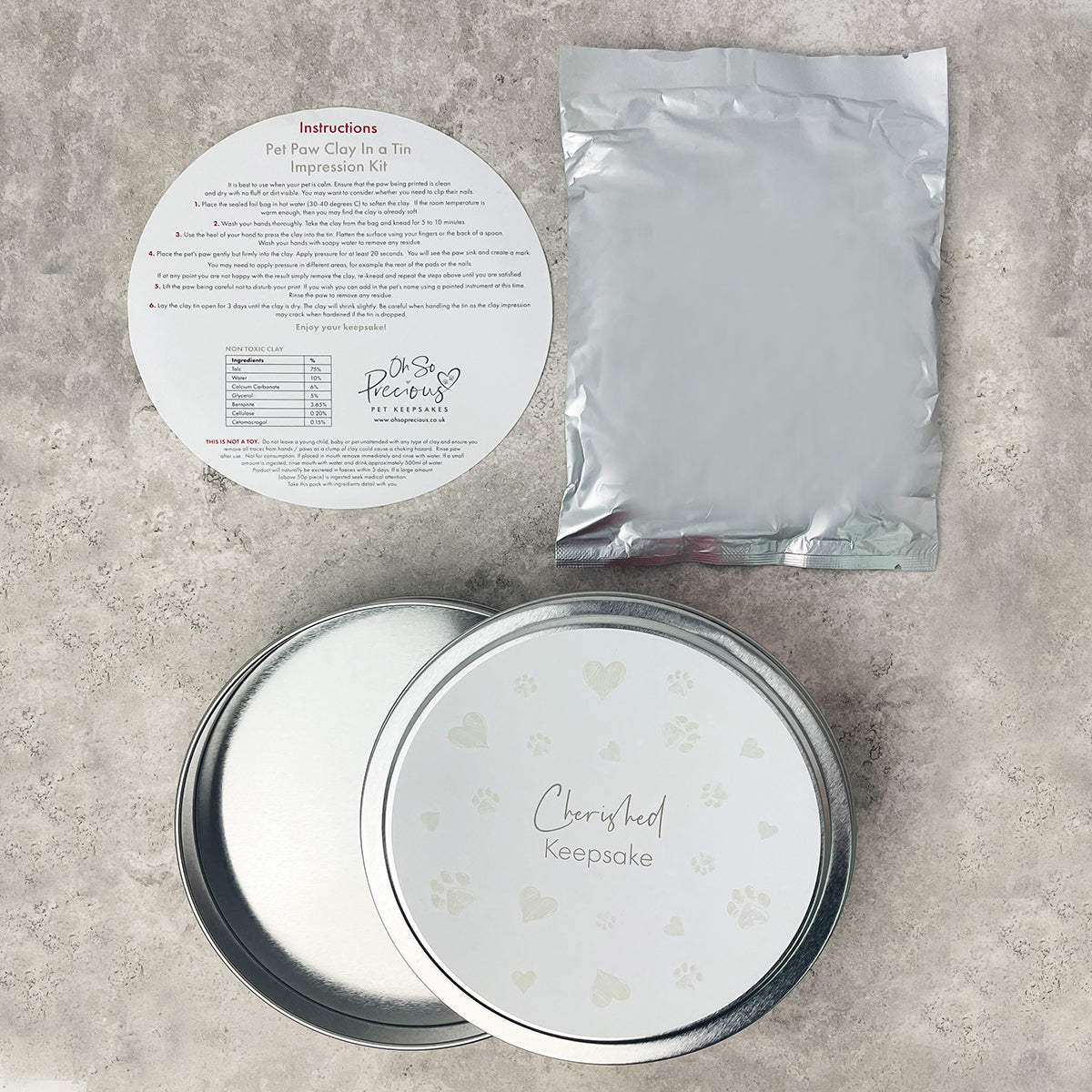 Pet paw print kit with a round container, packaging, and instructions on a gray surface.