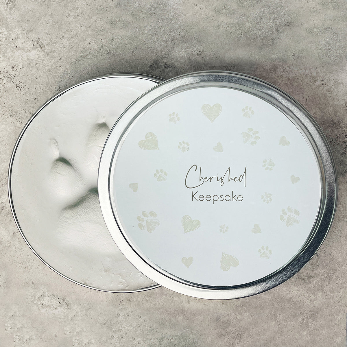 Round silver container with 'Cherished Keepsake' text on a textured surface