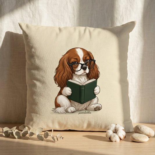 Pillow with a king charles cavalier dog reading a book design on a wooden surface.