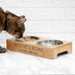 Cat eating from a wooden pet bowl named 'Bertie's Bowl' on a white marble surface.