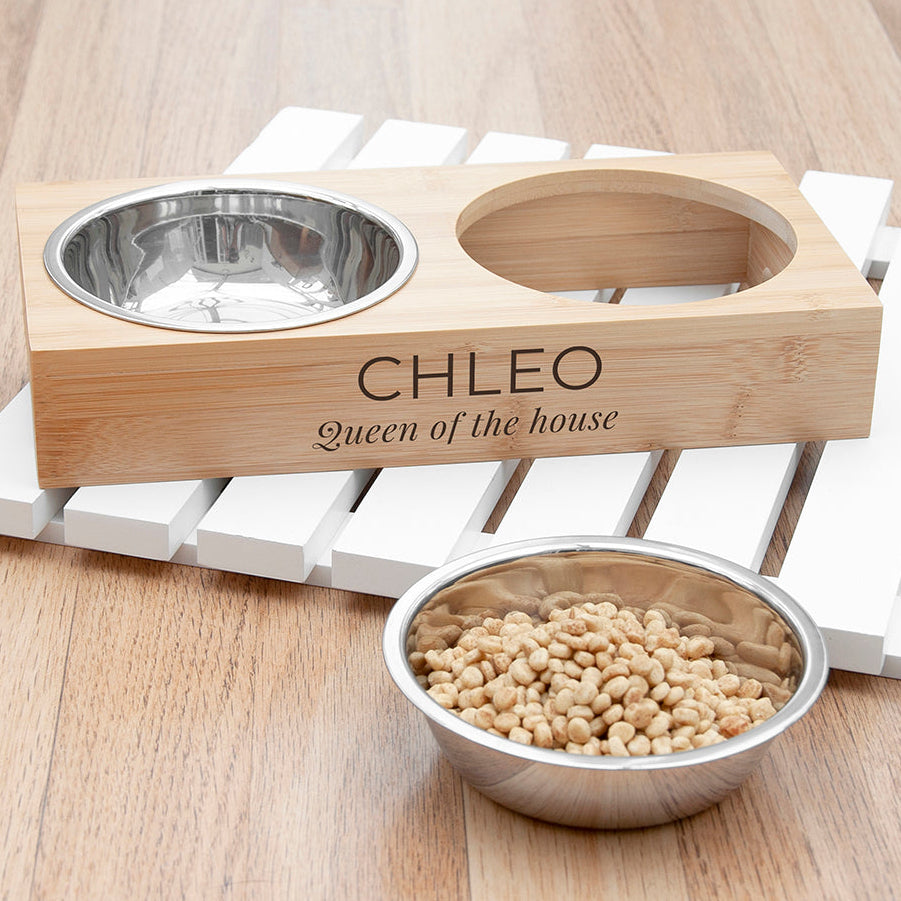 Wooden pet bowl stand with engraved name 'CHLEO' and a metal bowl filled with food on a wooden surface.