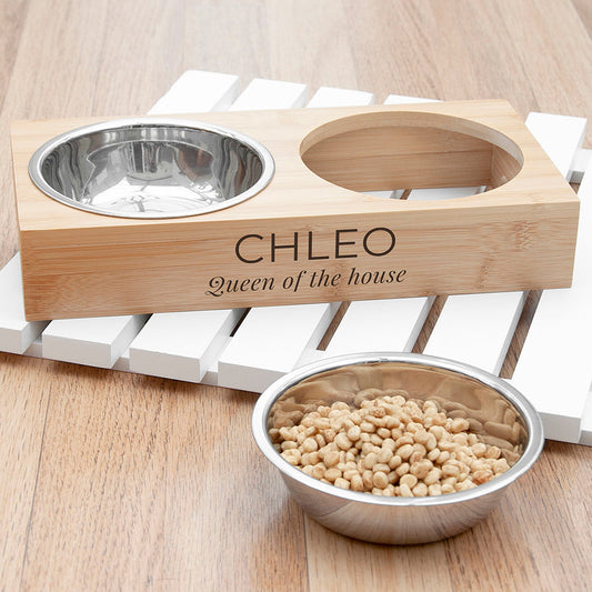 Wooden pet bowl stand with engraved name 'CHLEO' and a metal bowl filled with food on a wooden surface.