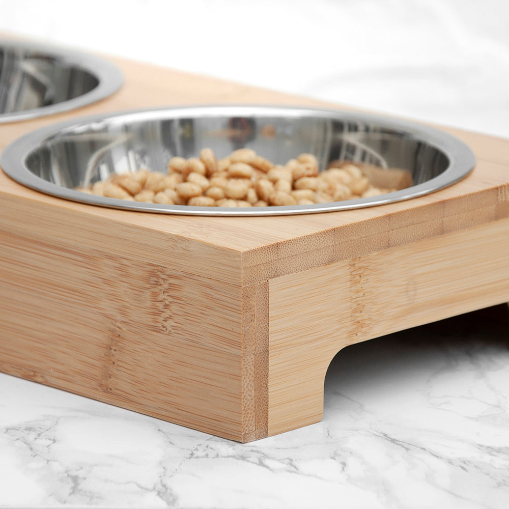 Wooden pet feeder with two metal bowls containing food on a marble surface