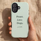 A hand holds a pale mint green phone case with the text 'Peace. Love. Dogs