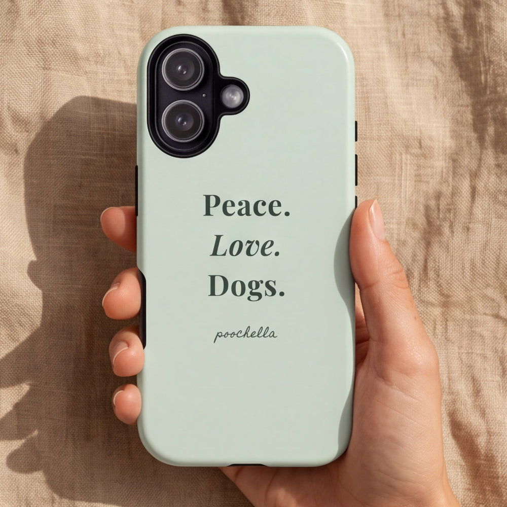 A hand holds a pale mint green phone case with the text 'Peace. Love. Dogs