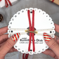 Kumihimo disk with red braided cord held by hands, with Christmas decorations in the background.
