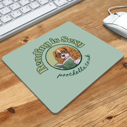 Mouse pad with a dog illustration and text 'Reading is Sexy' on a wooden desk with a keyboard and mouse.