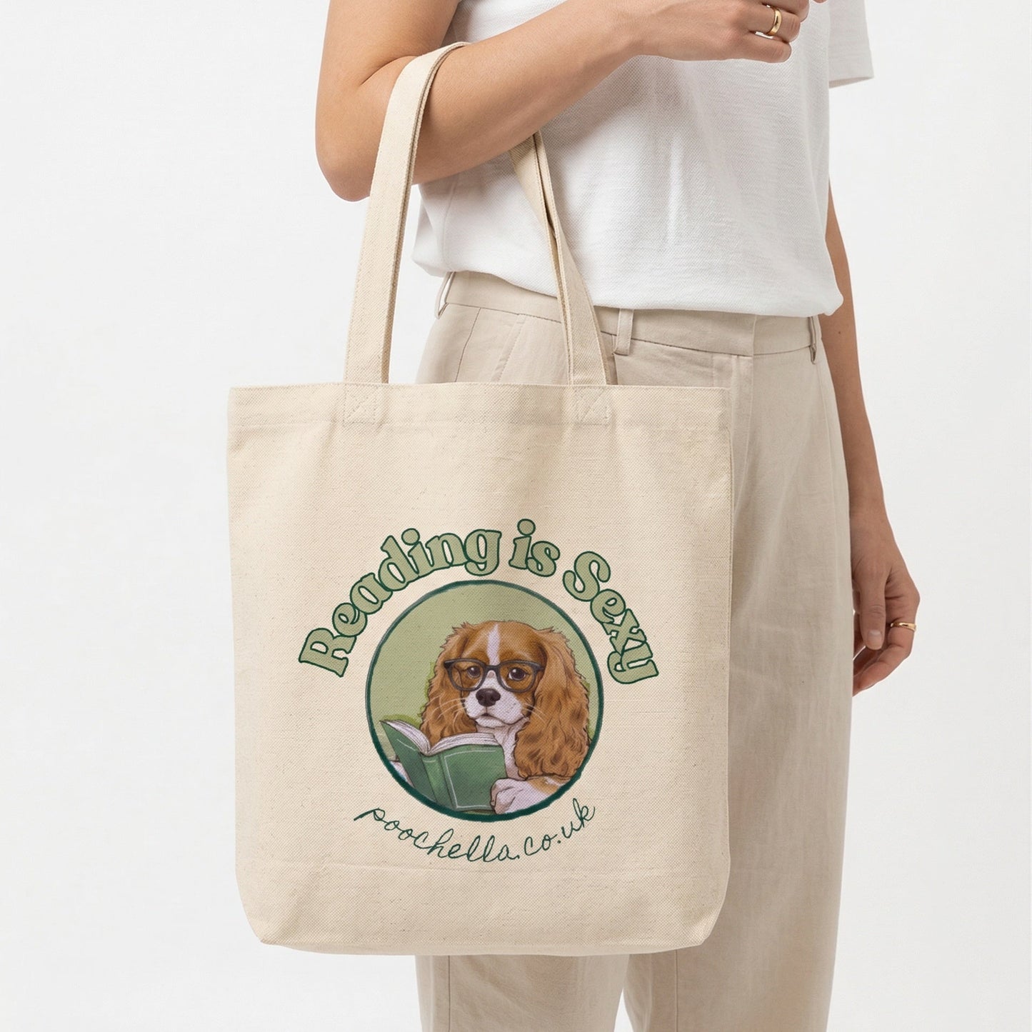 Tote bag with a dog illustration and text 'reading is sexy'  held by a person on a white background