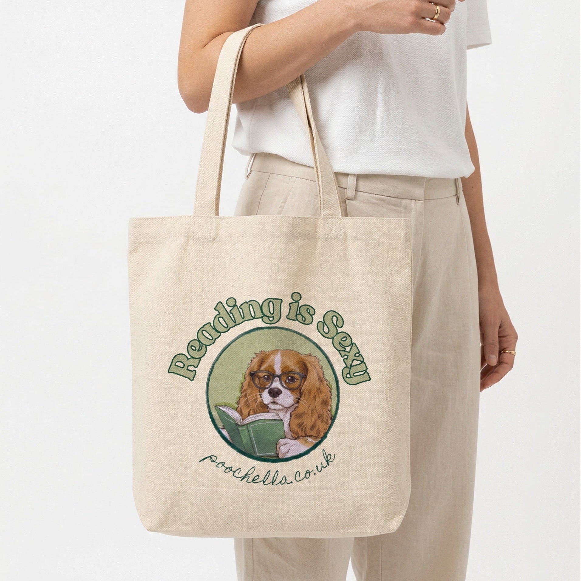 Tote bag with a dog illustration and text 'reading is sexy'  held by a person on a white background