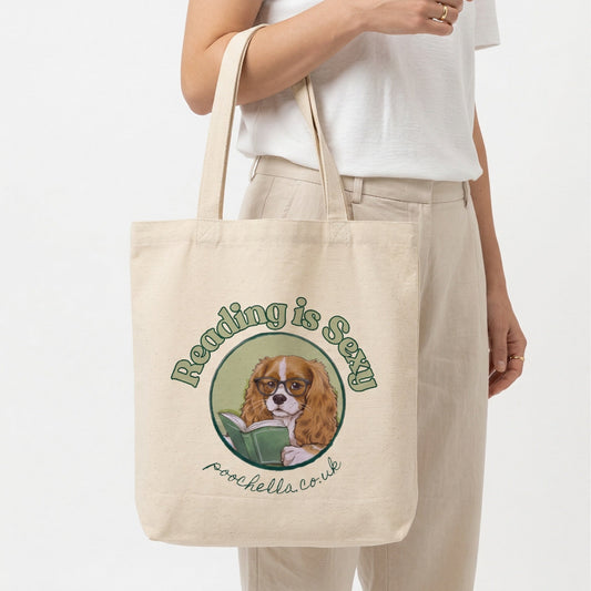Tote bag with a dog illustration and text 'reading is sexy'  held by a person on a white background