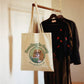 Tote bag with a dog illustration and text hanging on a rack with clothes.