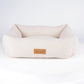 A cream-colored sheepskin pet bed with a small brown leather 'Scruffs' brand patch, displayed on a white circular platform against a white background.