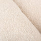 A close-up of a textured cream-colored fabric, showing a soft, looped terry cloth or bouclé texture with a diagonal fold.