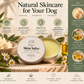A round tin of Poochella Kindred Skin Salve for dogs is displayed on a rustic wooden surface with white flowers and a green informational panel. The tin contains pale yellow balm, and the graphic includes text highlighting key ingredients like shea butter, hemp oil, and vitamin E.