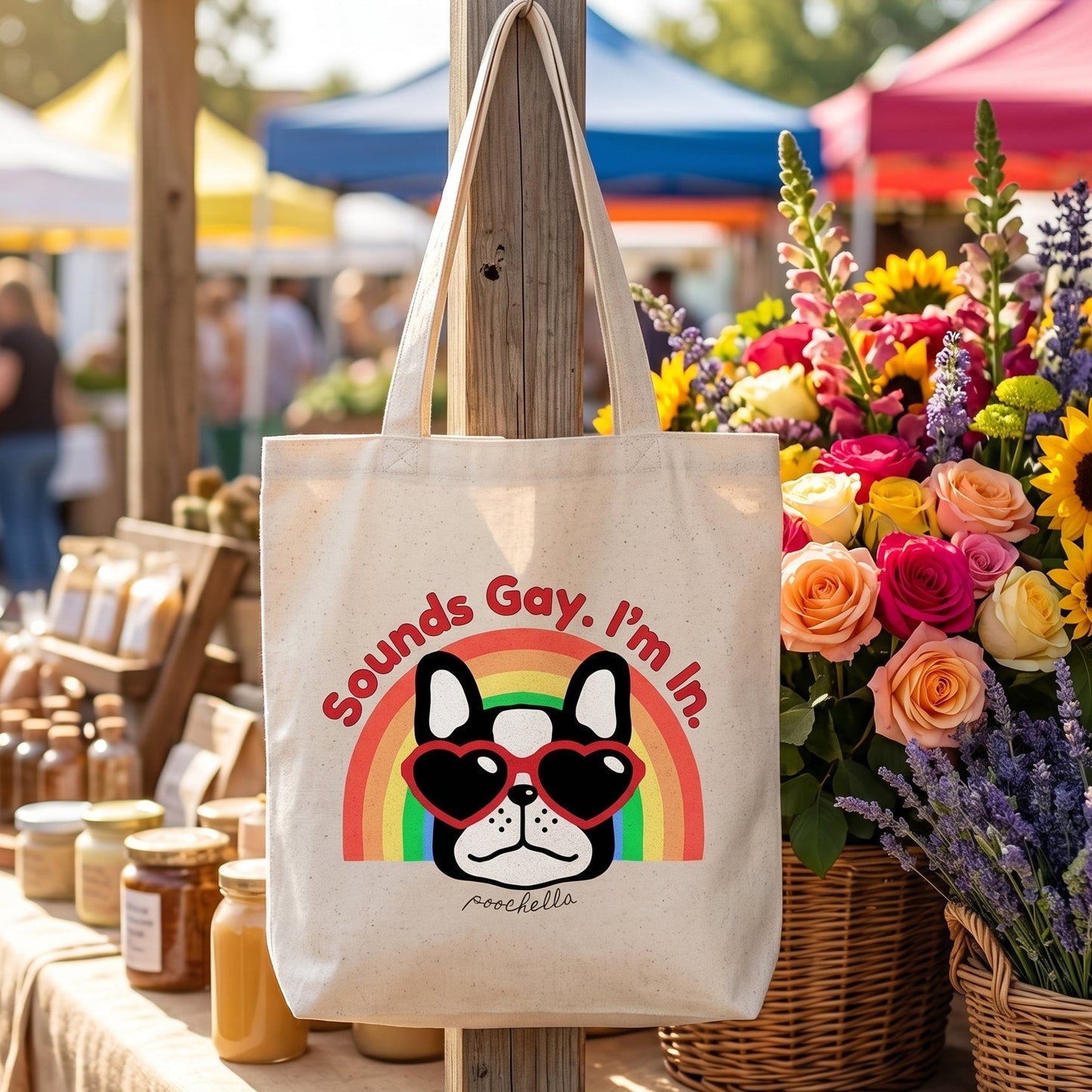 Tote bag with a dog graphic and text at an outdoor market stall with flowers and jars.