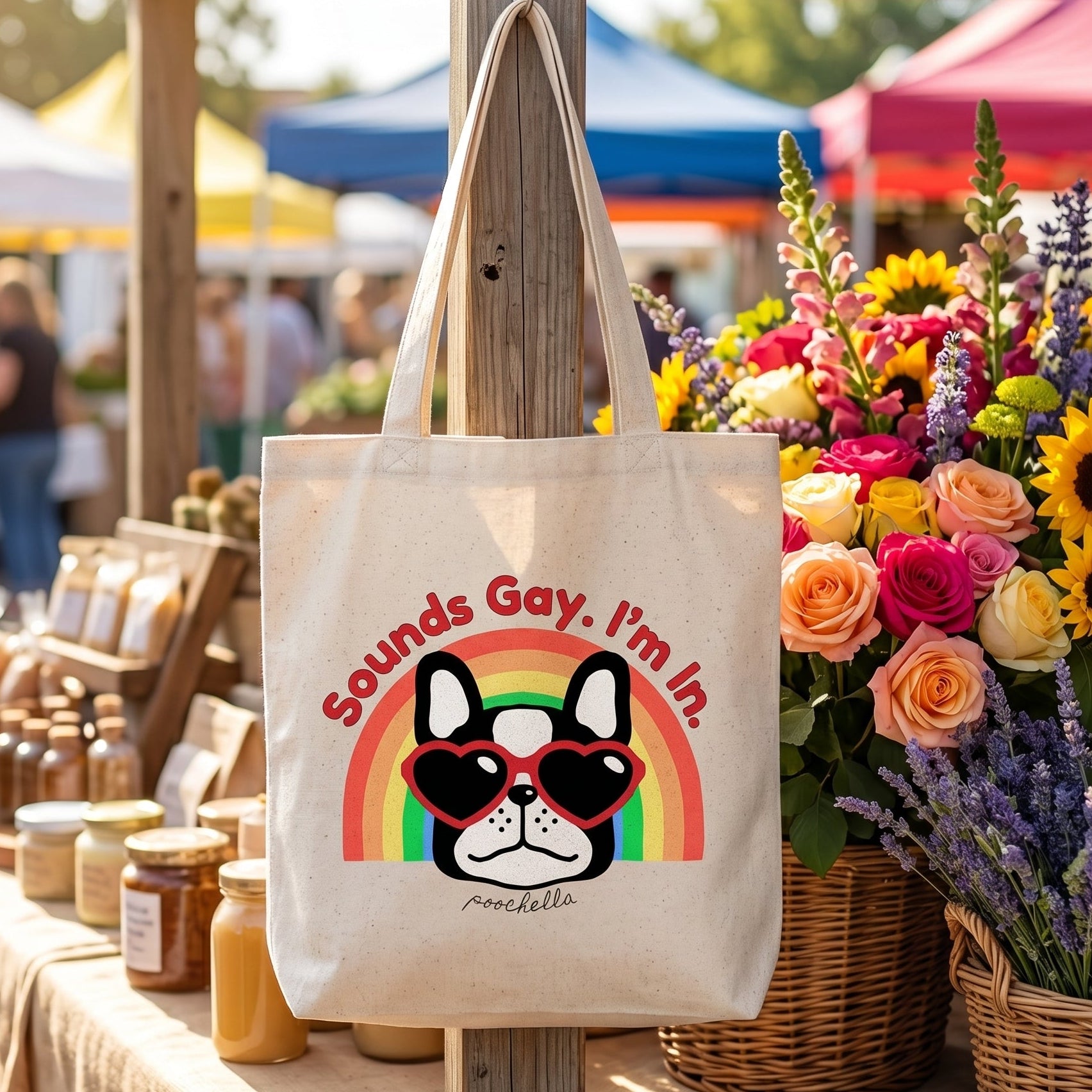 Tote bag with a dog graphic and text at an outdoor market stall with flowers and jars.