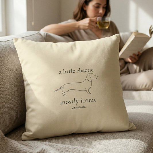 Woman reading a book on a couch with a decorative pillow featuring a dachshund illustration and text.