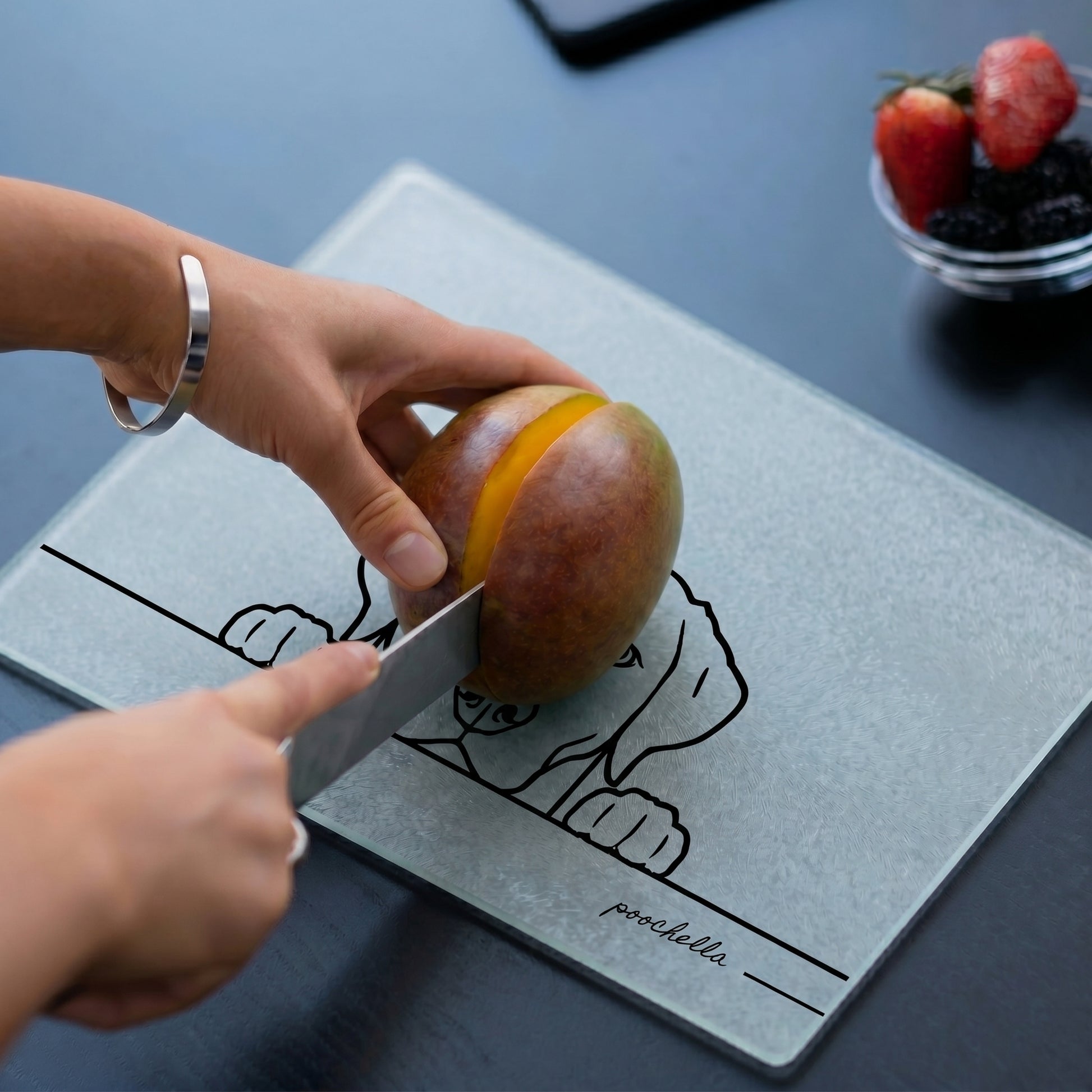 Person cutting a mango on a glass cutting board with labrador dog design
