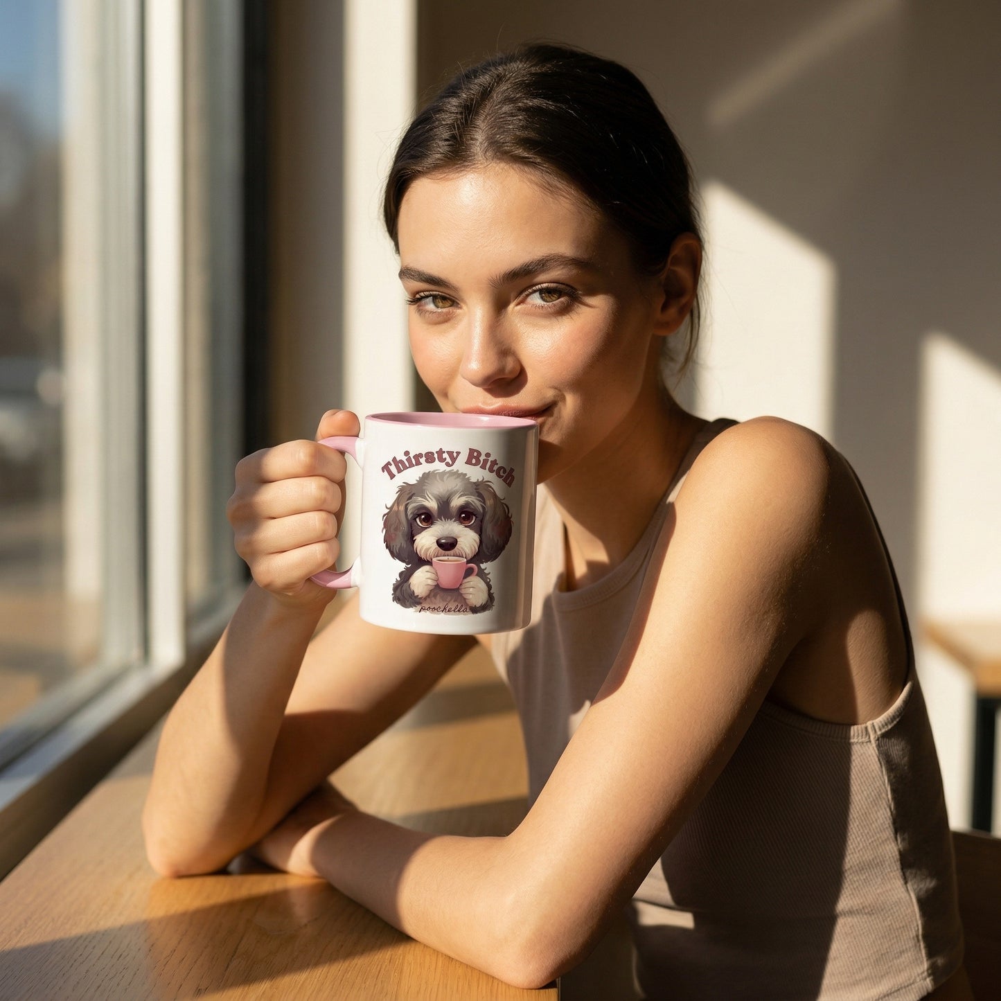 Woman holding a mug with a dog design and text, sitting by a window.