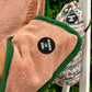 Close-up of a pink towel with a black label, with another towel and a bag in the background.