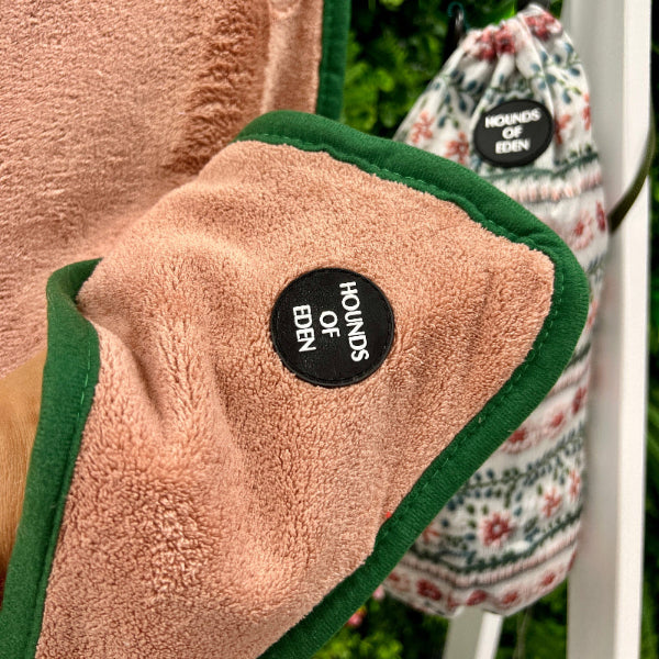 Close-up of a pink towel with a black label, with another towel and a bag in the background.