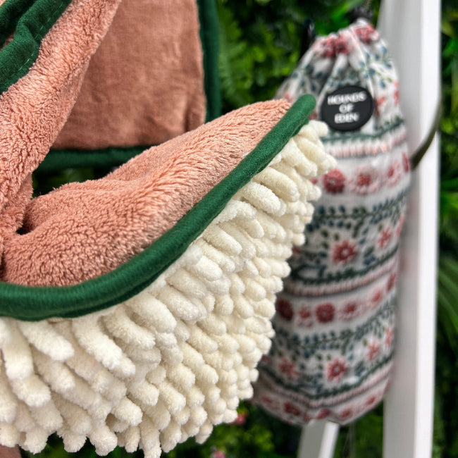 Close-up of a pink and green textured dog towel with a white pom-pom trim, hanging on a rack.
