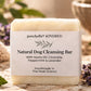 A bar of poochella KINDRED Natural Dog Cleansing Bar with a white paper label, styled on a rustic stone surface with lavender flowers, mint leaves, and a woven basket in the background.
