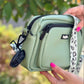 Light green crossbody bag held by a person with a blurred natural background