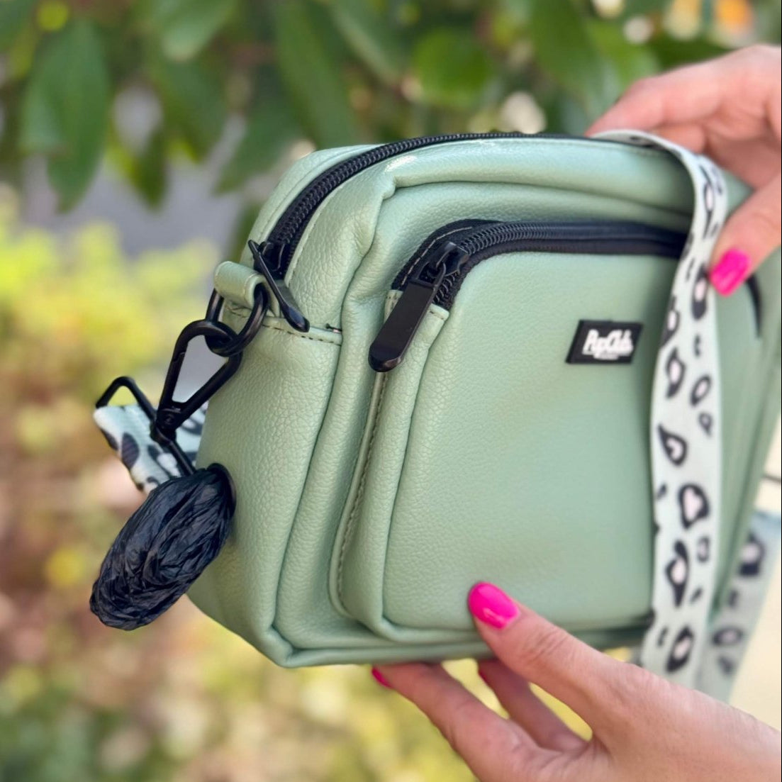 Light green crossbody bag held by a person with a blurred natural background