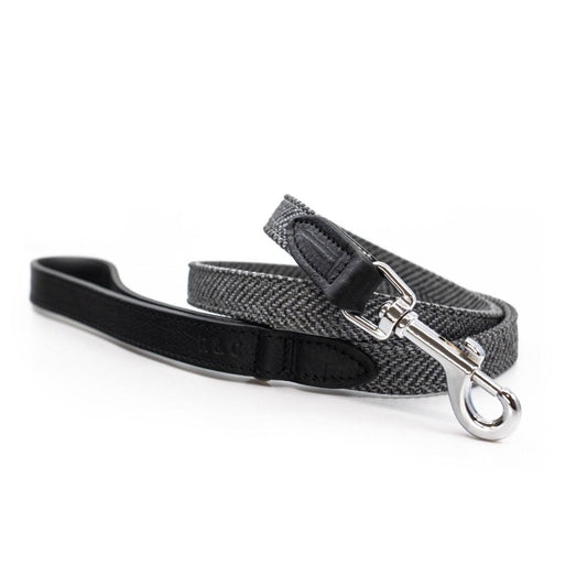 A black and gray herringbone patterned dog leash with a black leather handle and silver metal snap hook, displayed on a clean white background.